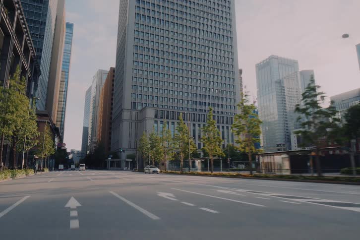 A serene point-of-view drive through the nearly empty streets of downtown Tokyo, passing by modern architectural skyscrapers in the morning light