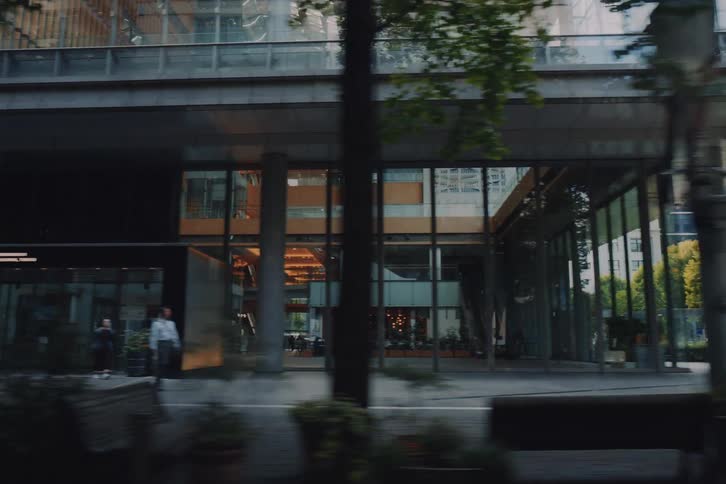 A slow-motion drive-by view of a modern urban street in Tokyo, lined with green trees, contemporary architecture, and passing traffic
