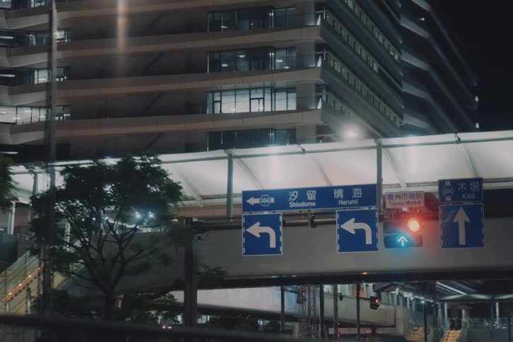 A dreamy tracking shot from a vehicle driving through a modern city at night, passing under overpasses and by contemporary architecture
