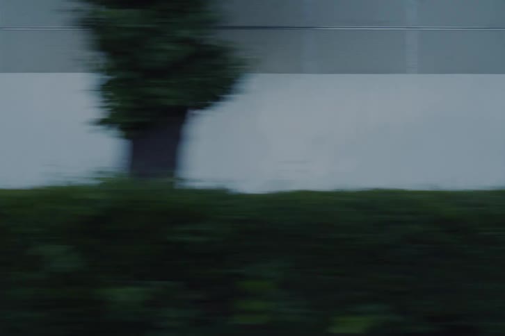 A cinematic side-scrolling view from a vehicle driving through the streets of a modern Japanese metropolis