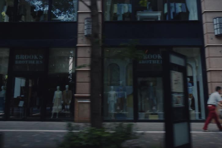 A cinematic tracking shot captures the storefronts, architecture, and pedestrians along a modern Tokyo street as day transitions to evening