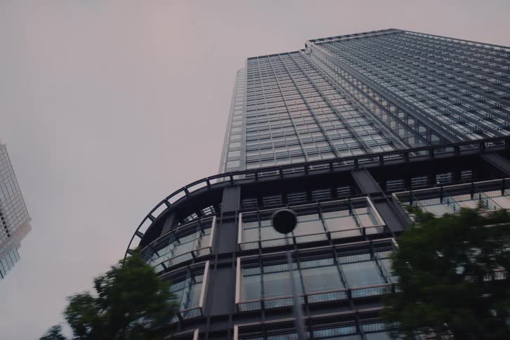 A low-angle tracking shot of a modern, glass skyscraper in a metropolitan city on an overcast day
