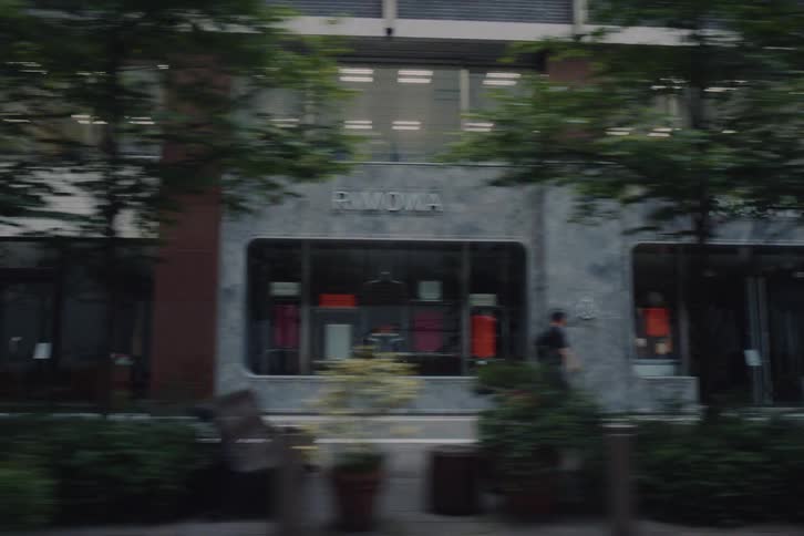 A smooth tracking shot from a moving vehicle captures the architecture, storefronts, and pedestrians along a quiet city street in Tokyo, Japan