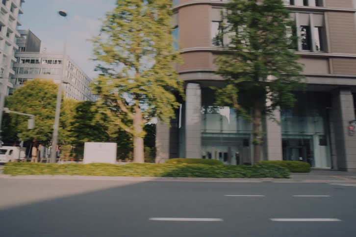 A smooth vehicle point-of-view tracking shot driving through the streets of Tokyo, transitioning from twilight to sunny morning, passing by diverse architecture