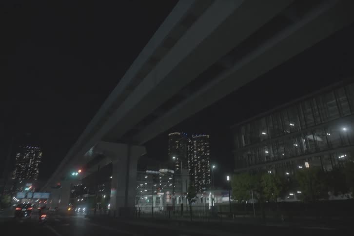 Driving through the quiet streets of a modern city at night, passing under an elevated highway