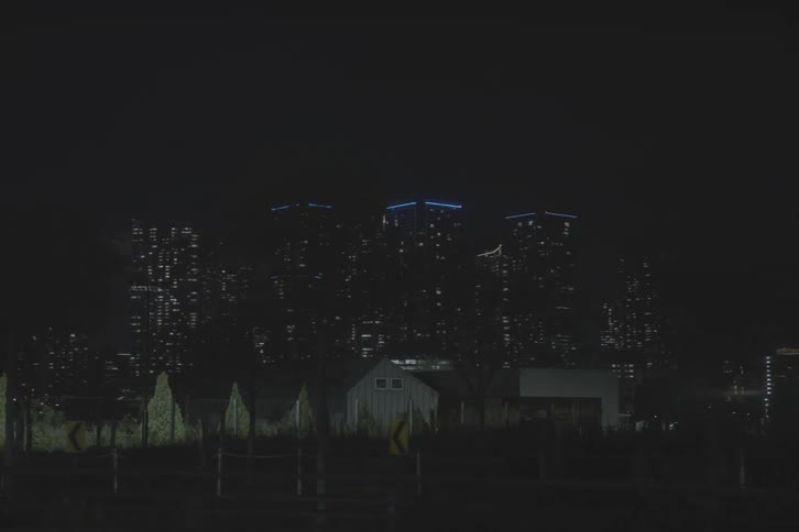 A smooth tracking shot from a vehicle captures the sights of a modern city at night, from a quiet gas station to the glowing skyline