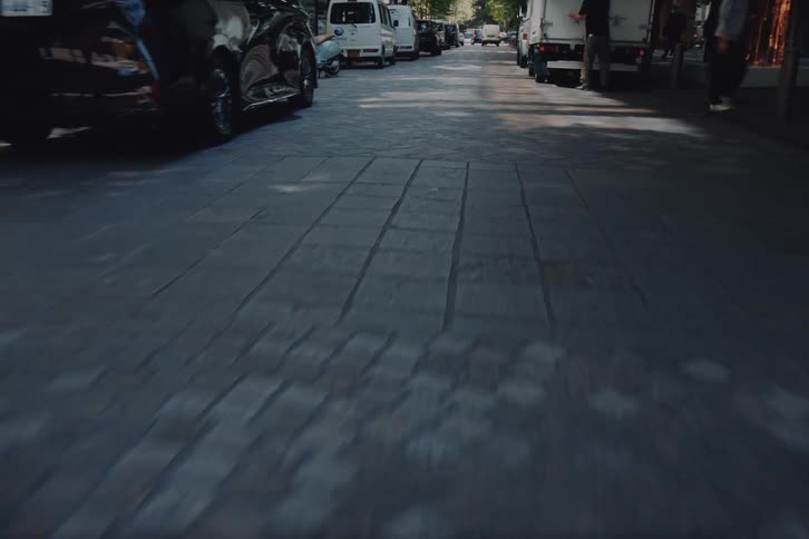 A dynamic POV shot moving along a city street, tilting down from a modern building to a low-angle view of the pavement and crosswalk