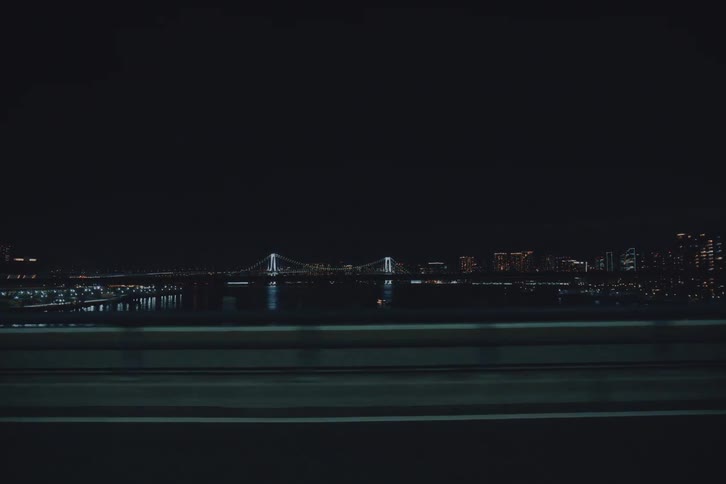 A cinematic point-of-view shot while driving through the streets of Tokyo at night, revealing the illuminated Rainbow Bridge and city skyline