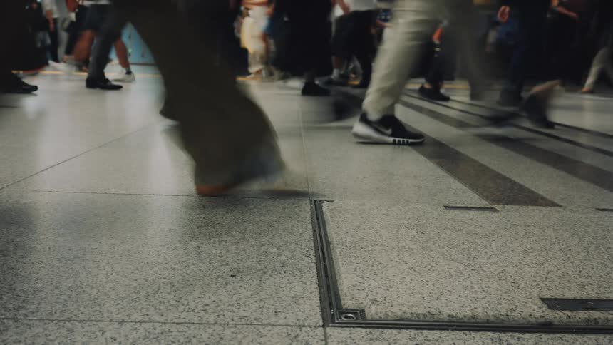 A low-angle time-lapse captures the hurried steps of a crowd of commuters walking through a busy station