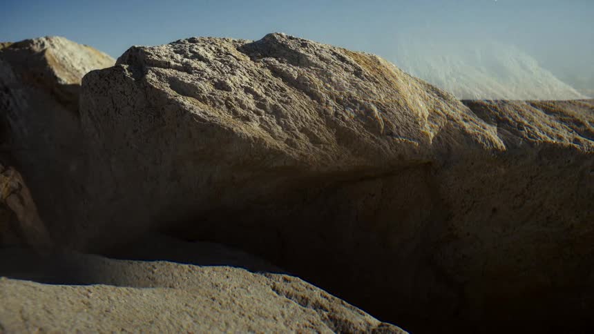 Windy gusts blow sand across a sunlit rock in a dry, desolate landscape