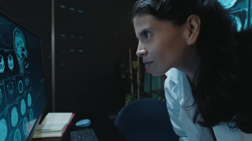 A female doctor intently studies brain scans on a computer monitor and smiles with relief upon making a diagnosis