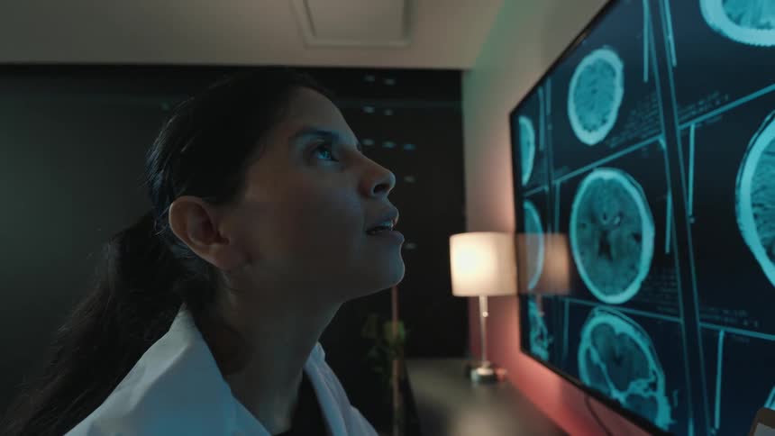 A dedicated female doctor analyzes brain scans on a large screen, her expression turning to a hopeful smile after making a discovery
