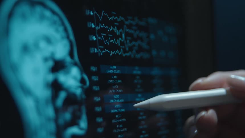 A doctor or researcher uses a stylus to closely examine a patient's brain scan and brainwave data on a digital screen