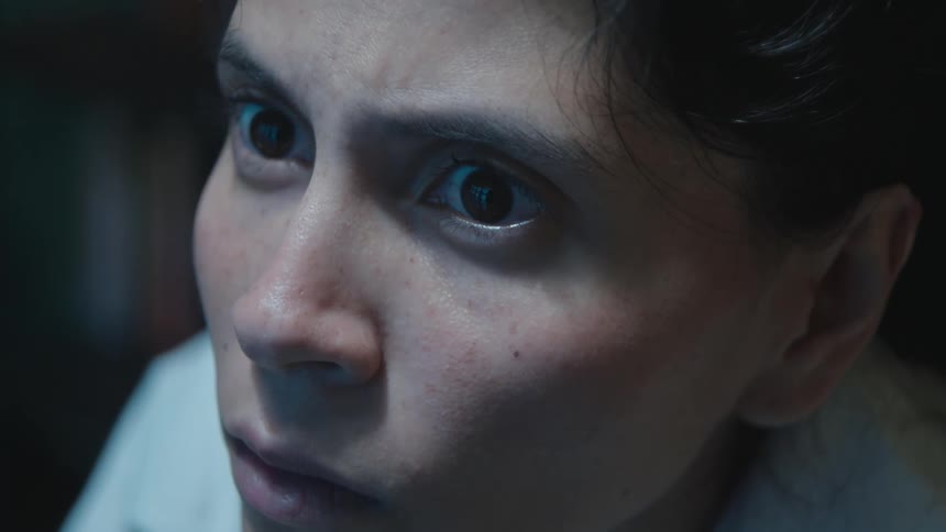 An extreme close-up of a woman's eyes widening in fear and shock while watching something on a screen in the dark