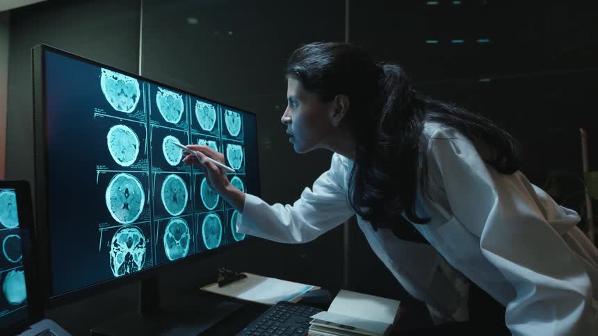 Focused neurologist points at a patient's CT brain scan on a high-tech computer screen in a modern, dark office