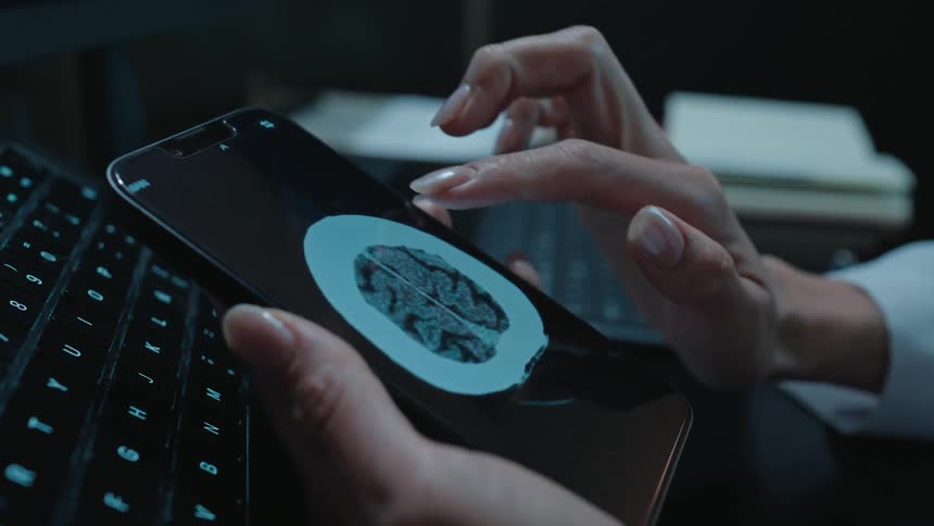 A medical professional carefully analyzes a patient's brain CT scan on a smartphone in a dark room