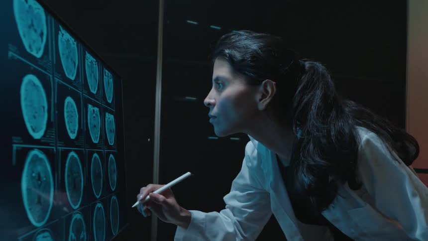 Slow motion footage shows a female doctor analyzing brain CT scans on a large interactive screen in a dark lab