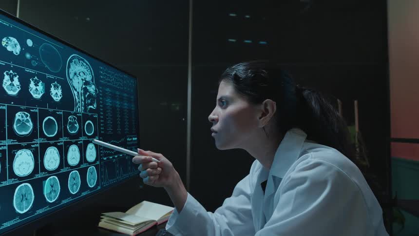 A focused neurologist points with a stylus while examining a patient's brain CT scan on a high-tech monitor in a modern lab