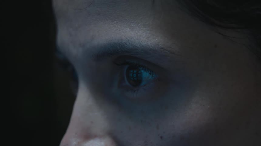 Extreme close-up of a person's eye reflecting a ring light as they focus intently in a dark room