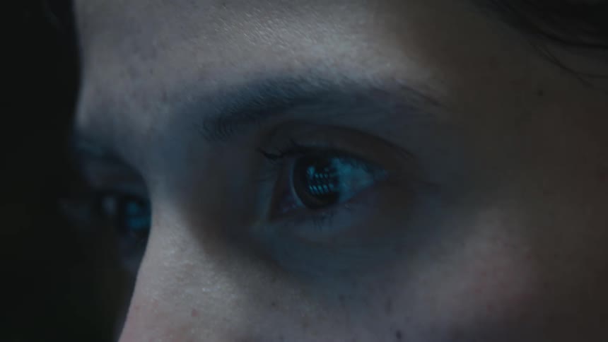 Extreme close-up of a person's eye reflecting data scrolling on a computer monitor in a dark room
