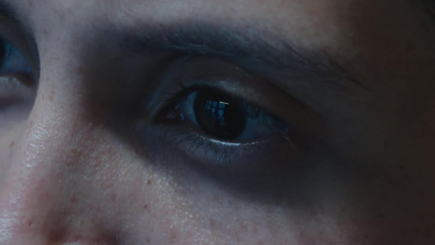 Extreme close-up of a human eye blinking in the dark, with a computer screen reflected in the pupil