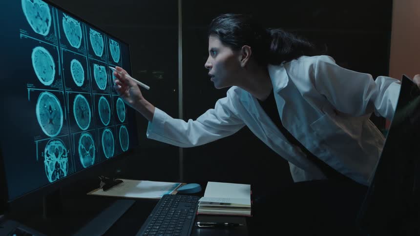 Slow motion of a female doctor in a dark room intensely examining brain scans on a computer screen