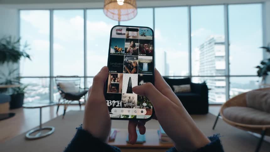 A first-person view of a person scrolling through a photo gallery on their smartphone in a modern apartment with a city view