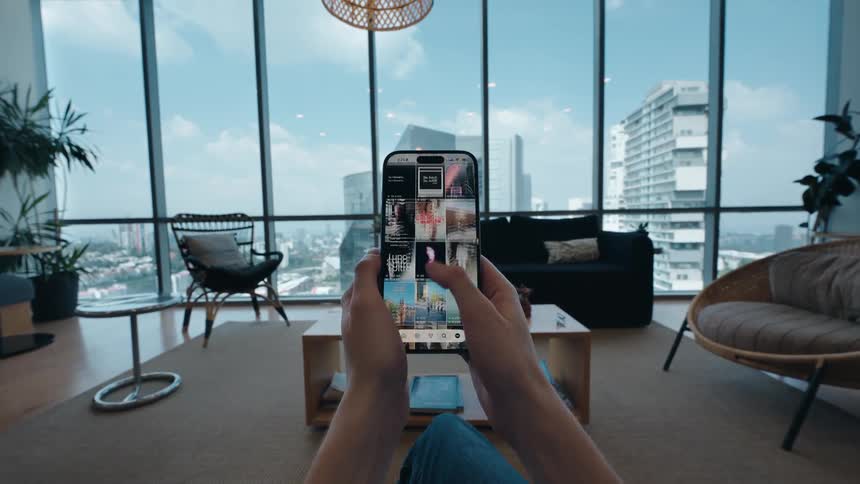 A first-person view of someone scrolling through a social media photo feed on their smartphone in a modern high-rise apartment