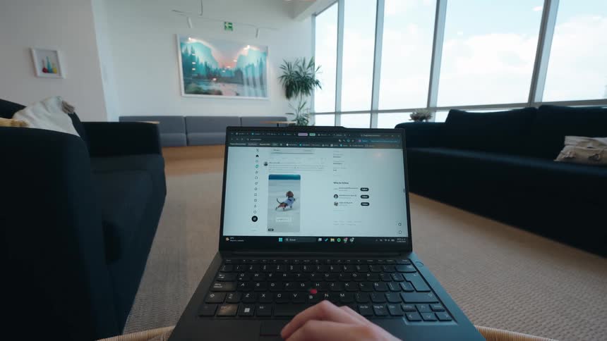 A first-person view of scrolling through a social media feed on a laptop in a bright, contemporary office lounge