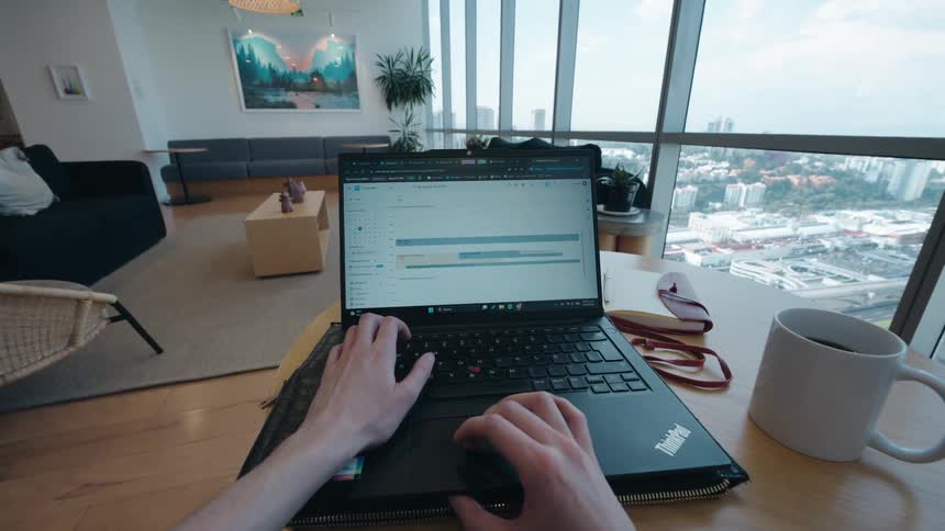 POV shot of a remote worker typing on a laptop in a modern apartment with a panoramic city view