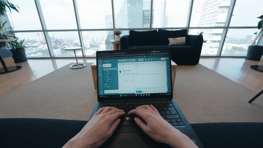 First-person perspective of hands typing on a laptop in a modern high-rise apartment with a city view