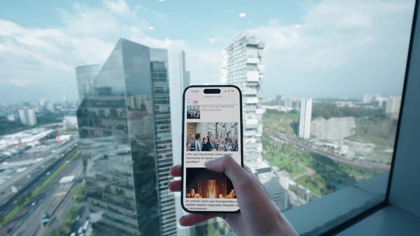 A person scrolls through the news on their smartphone from a high-rise building with a stunning view of a modern cityscape