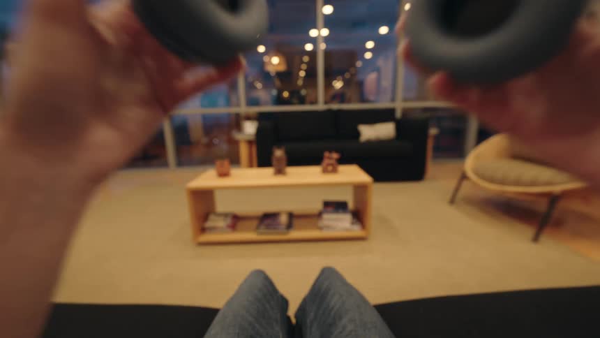 A first-person point of view of someone putting on headphones while relaxing on a couch in a modern living room at night