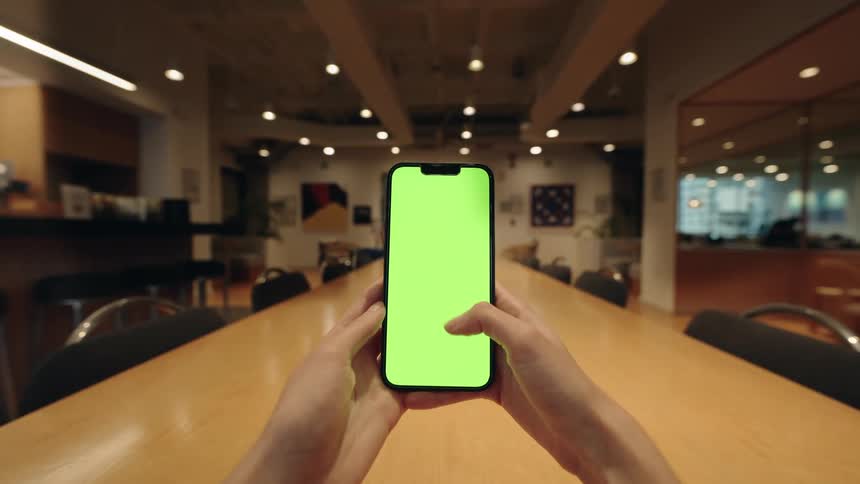 First-person view of a person using a smartphone with a green screen, performing various gestures at an office table
