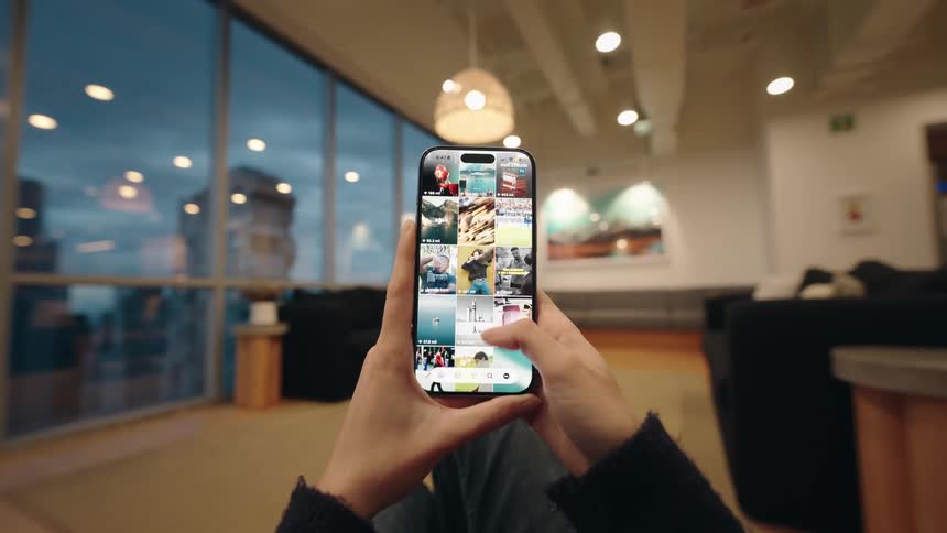 A close-up, first-person view of a person scrolling endlessly through a social media photo feed on their smartphone while relaxing indoors