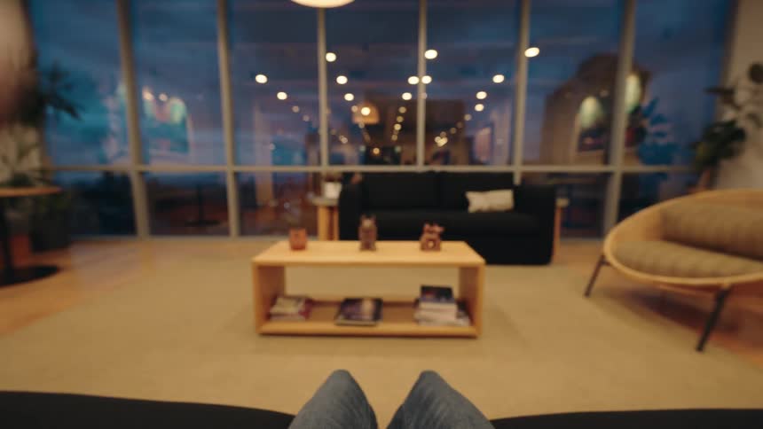 First-person point of view of a person putting on wireless headphones in a modern, cozy living room at night