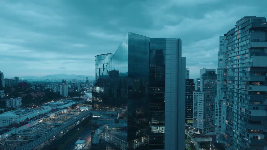 A modern metropolis with glass skyscrapers reflecting a dramatic, moody blue sky as traffic moves below at dusk