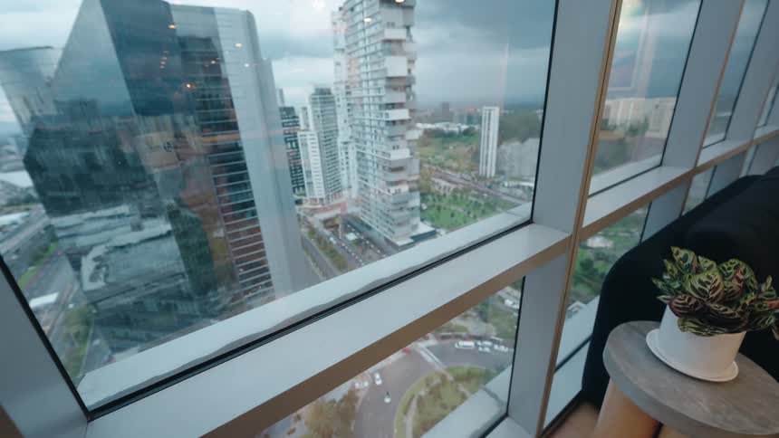 First-person perspective of a hand holding a coffee mug while overlooking a modern cityscape from a high-rise window
