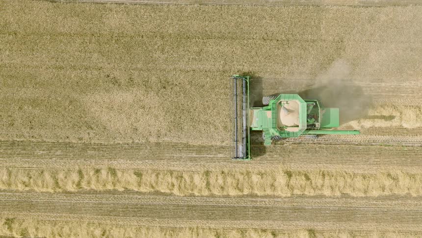 A top-down aerial view shows a modern green combine harvester reaping a golden crop in a large agricultural field