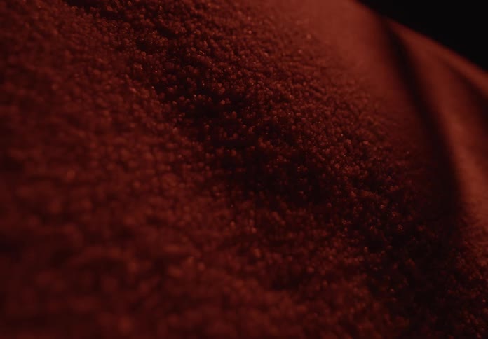 A dramatic macro shot of a beam of light moving across a textured, deep red powder, creating shifting shadows