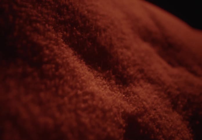 Red granular particles shift and flow like waves in a mysterious, abstract close-up