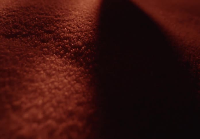 Dramatic warm light and shadow play across the textured surface of a dark red fabric in a slow-moving abstract macro shot