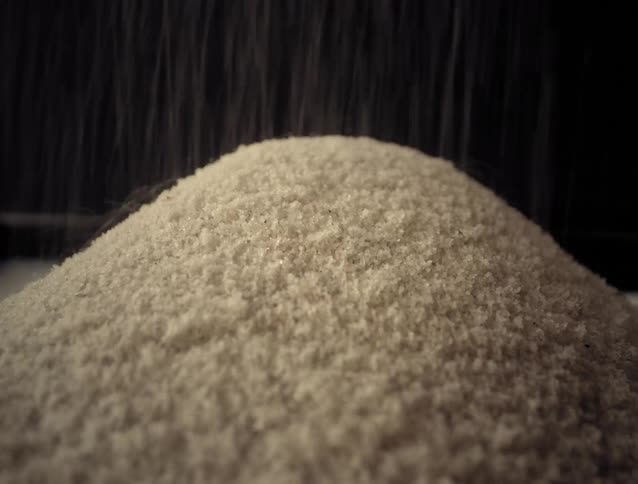 A close-up macro shot of coarse white salt being poured onto a growing pile against a dark background