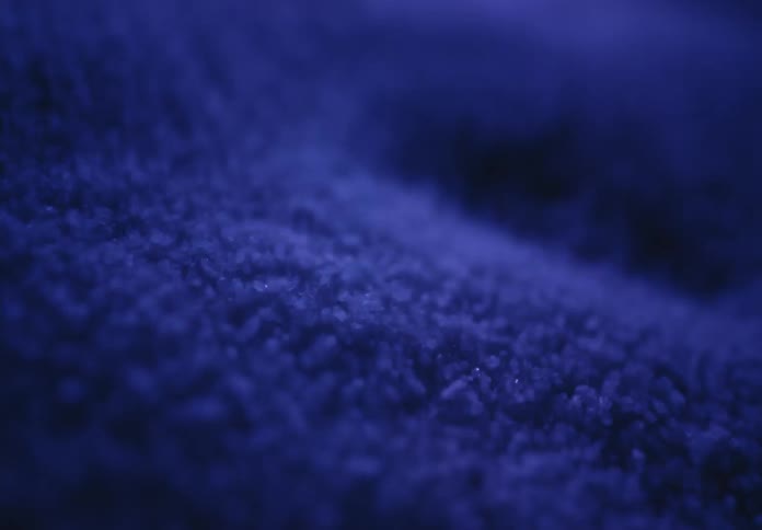 A slow, abstract macro pan across a soft, sparkling blue texture under moody lighting