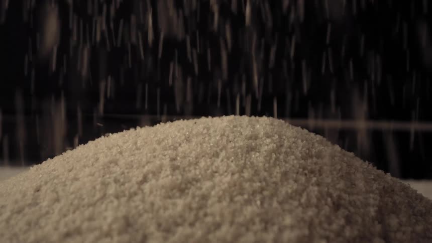 Slow motion macro shot of white semolina grains falling from above onto a growing pile against a dark background