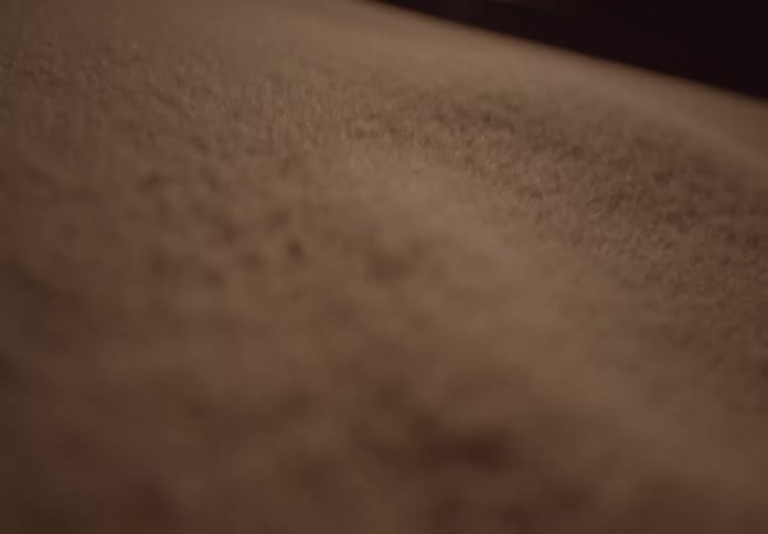 A mesmerizing slow-motion close-up shot of fine brown sand blowing across a textured surface
