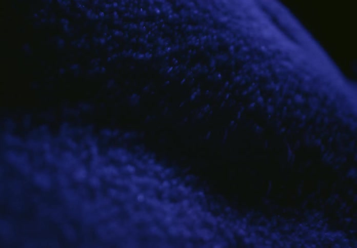 A macro shot captures hypnotic waves of blue particles moving in slow motion due to sound vibrations
