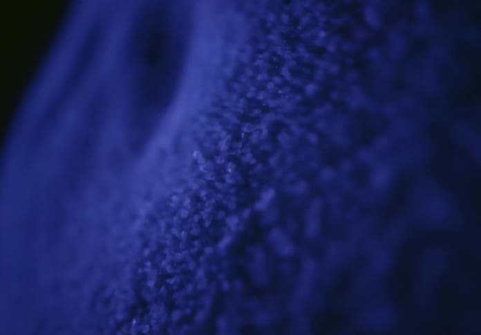 A moody, abstract macro shot of shimmering blue particles shifting and moving across a textured surface