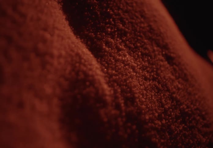 Macro close-up of red granular particles vibrating and shifting on a surface in warm, low light