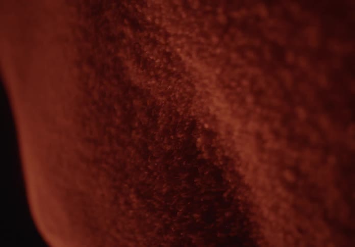 Vibrating red sand particles create abstract, mesmerizing patterns in a macro close-up shot